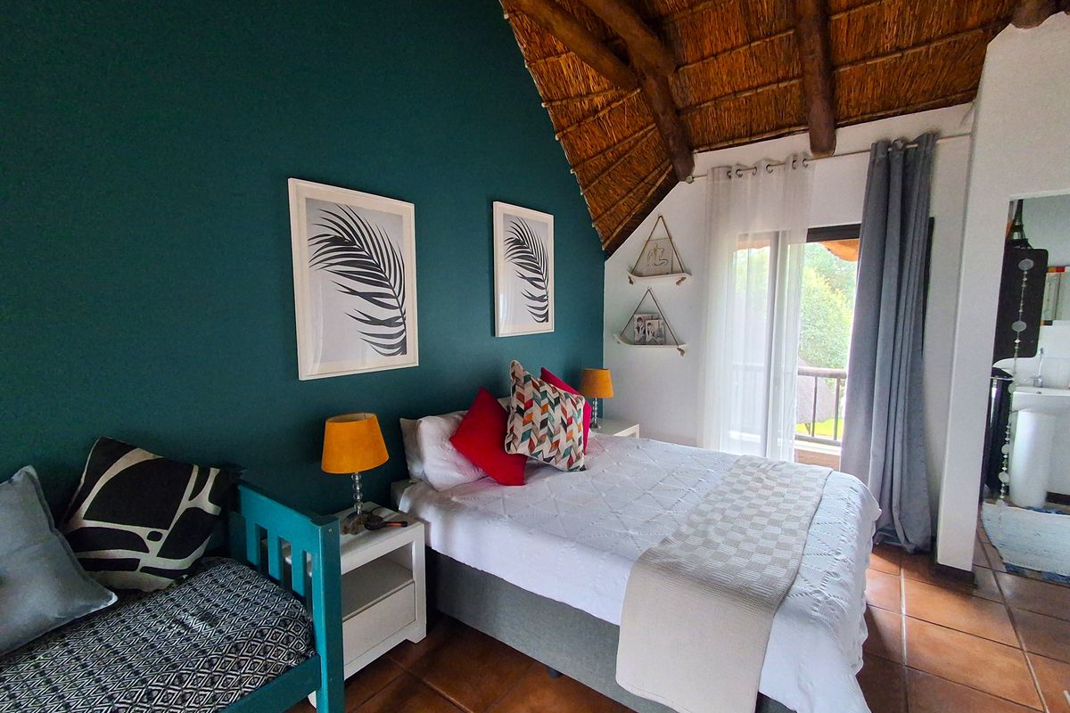 A cozy bedroom featuring a high vaulted thatched ceiling with exposed timber rafters, terracotta tiled flooring, and direct access to a private balcony.
