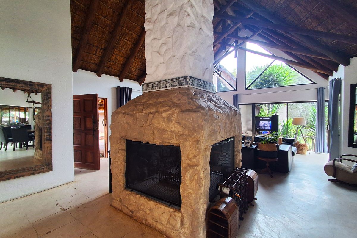 Spacious living area featuring a central stone fireplace, exposed timber trusses, and a high thatched ceiling with large windows providing natural light.