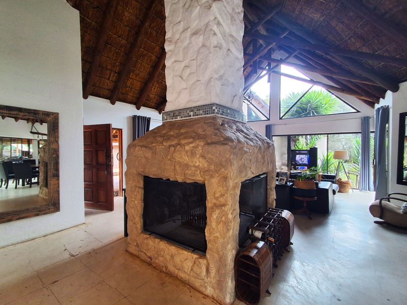 Spacious living area featuring a central stone fireplace, exposed timber trusses, and a high thatched ceiling with large windows providing natural light.
