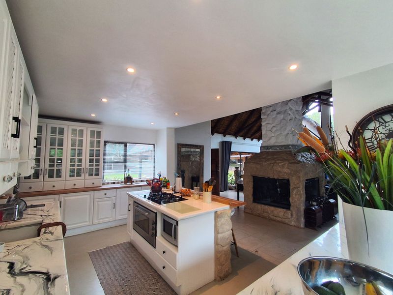 Spacious open-plan kitchen featuring white cabinetry, a central island with integrated appliances, and a prominent stone fireplace connecting to the living area.