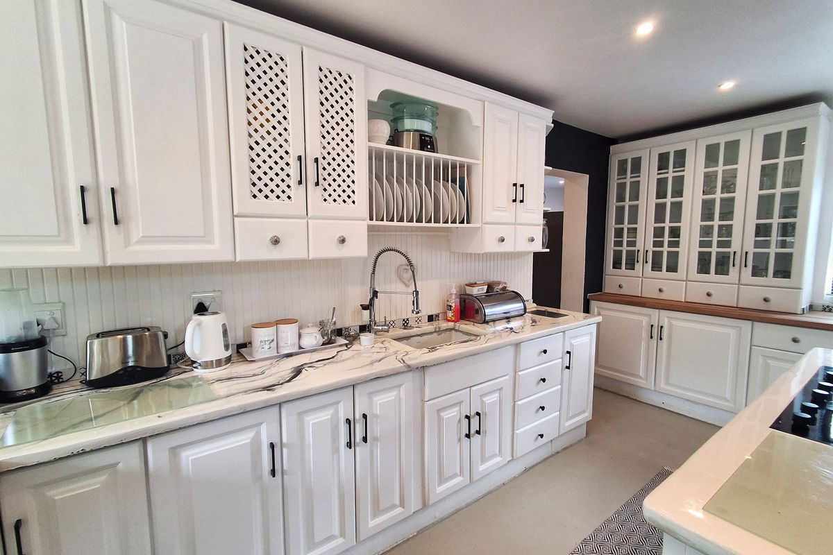 A bright kitchen featuring white cabinetry, marble-effect countertops, a built-in plate rack, and glass-front display cabinets, offering a classic and functional cooking space.