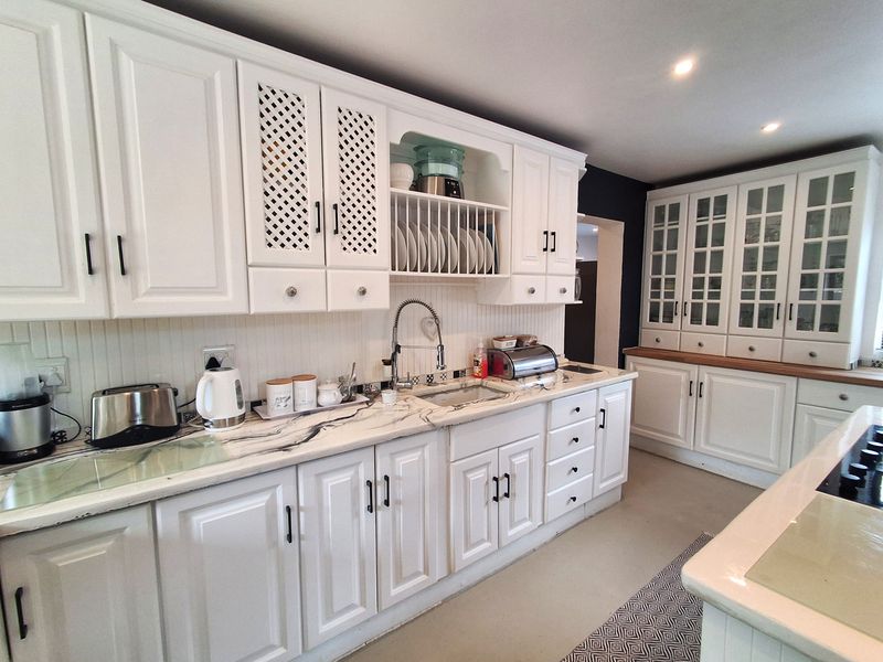 A bright kitchen featuring white cabinetry, marble-effect countertops, a built-in plate rack, and glass-front display cabinets, offering a classic and functional cooking space.