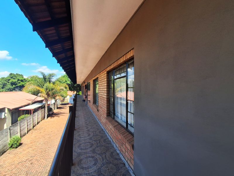 A covered outdoor balcony featuring tiled flooring, brick wall detailing, and a metal safety railing, overlooking the property grounds.