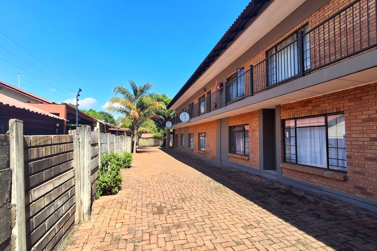 A well-maintained exterior view of a two-story brick residential building featuring a paved driveway, balcony access, and secure boundary walling.