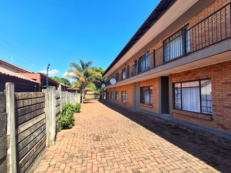 A well-maintained exterior view of a two-story brick residential building featuring a paved driveway, balcony access, and secure boundary walling.
