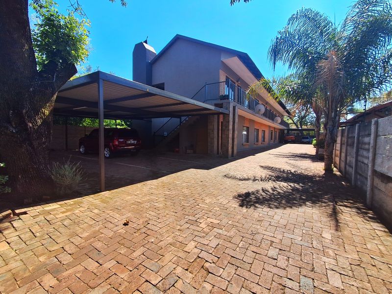 Front exterior view of the property featuring a brick paved driveway, covered carport, and an external staircase leading to an upper-level balcony.