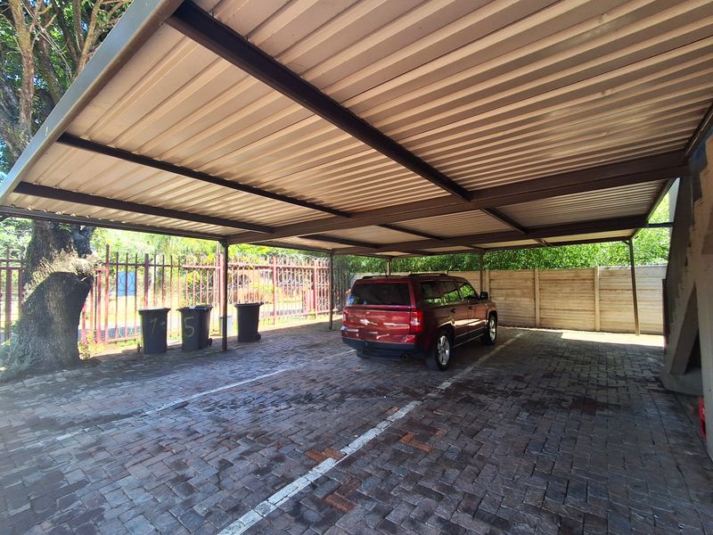 A covered carport area featuring a corrugated metal roof, steel support structure, and paved flooring, providing sheltered parking space.