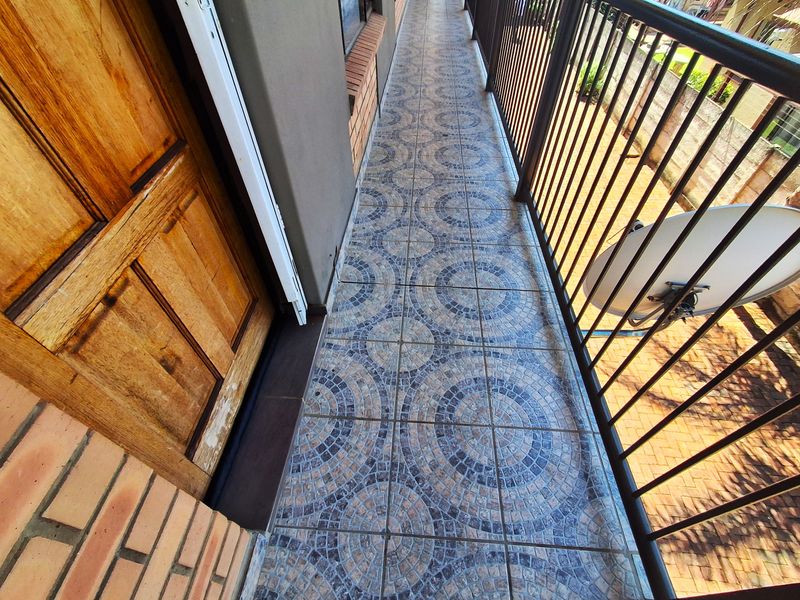 A narrow balcony featuring patterned tiled flooring, a metal safety railing, and a wooden entrance door.