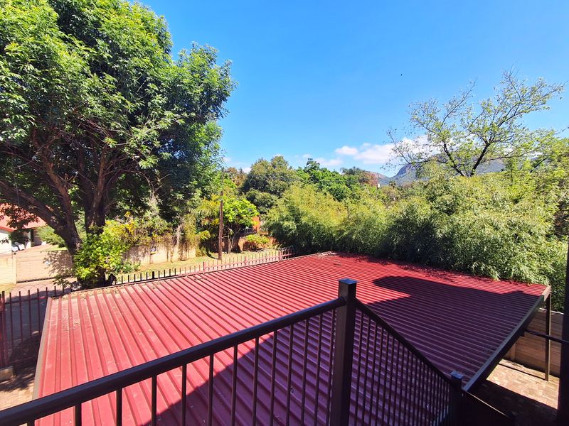 An elevated balcony area featuring a red metal roof and secure metal railing, overlooking a lush garden and surrounding landscape.