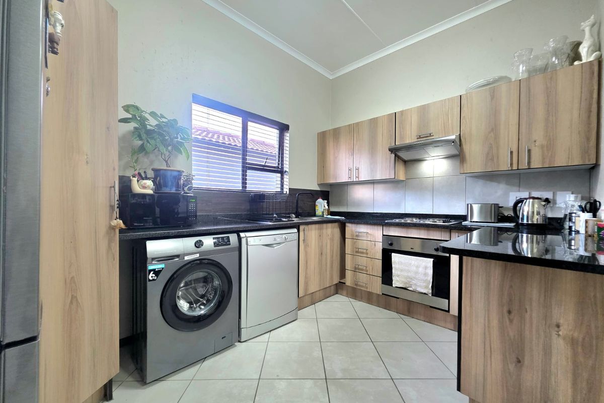 A functional kitchen featuring wood-look cabinetry, granite countertops, built-in oven, extractor fan, and tiled flooring with space for under-counter appliances.