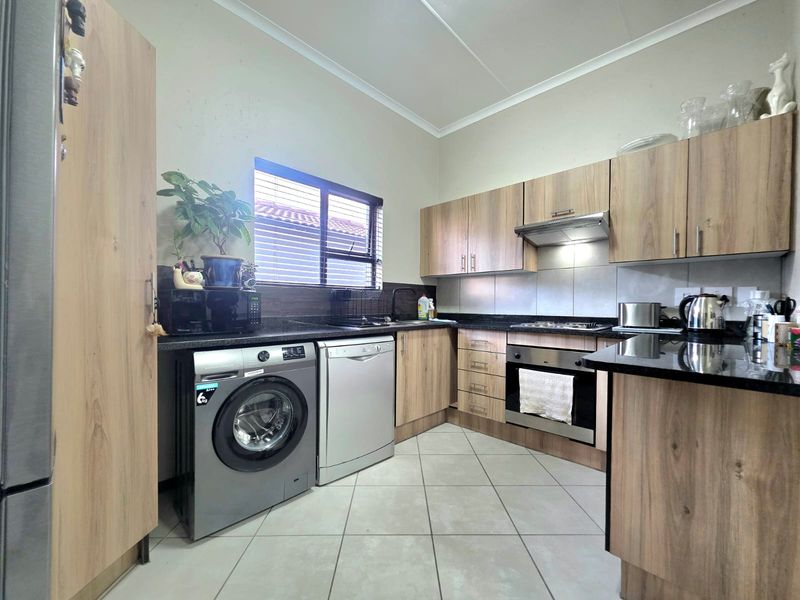 A functional kitchen featuring wood-look cabinetry, granite countertops, built-in oven, extractor fan, and tiled flooring with space for under-counter appliances.
