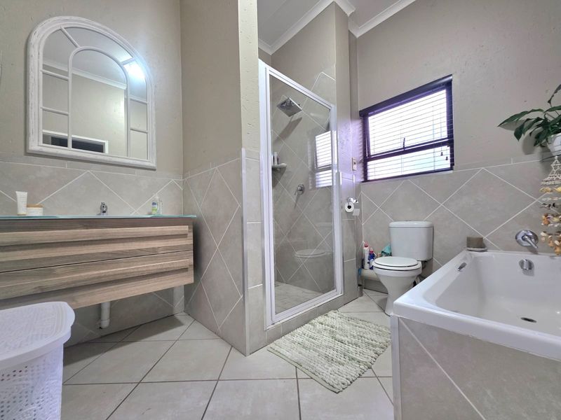 A well-maintained bathroom featuring a vanity cabinet, a separate shower enclosure, a bathtub, and neutral tiled finishes throughout.