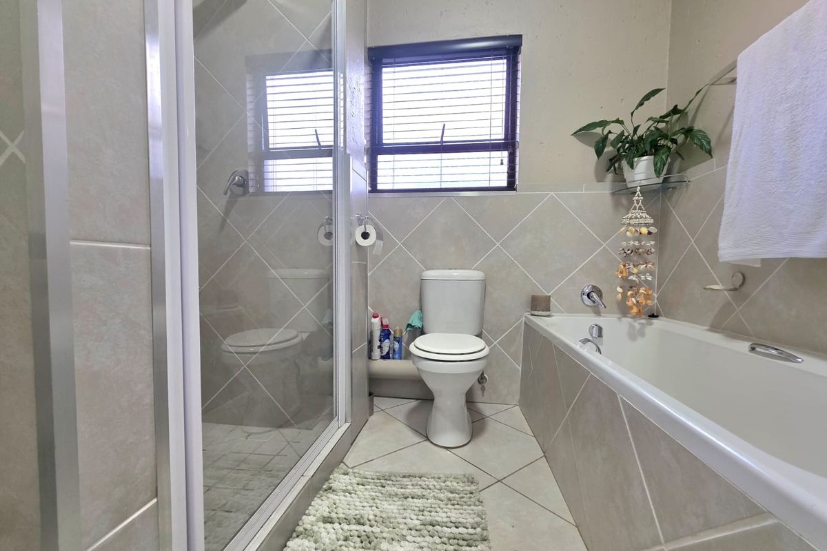A functional bathroom featuring a separate shower enclosure, a bathtub, and a toilet, finished with neutral wall and floor tiling.
