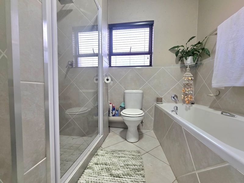 A functional bathroom featuring a separate shower enclosure, a bathtub, and a toilet, finished with neutral wall and floor tiling.