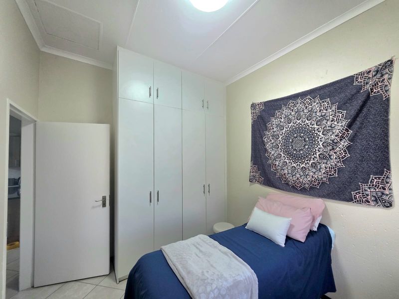 A functional bedroom featuring white built-in cupboards, tiled flooring, and a coved ceiling, providing a clean and practical living space.