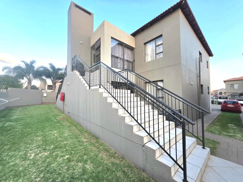 Rear view of the apartment building featuring an external staircase with metal railings leading to an upper level, set against a private lawn area.
