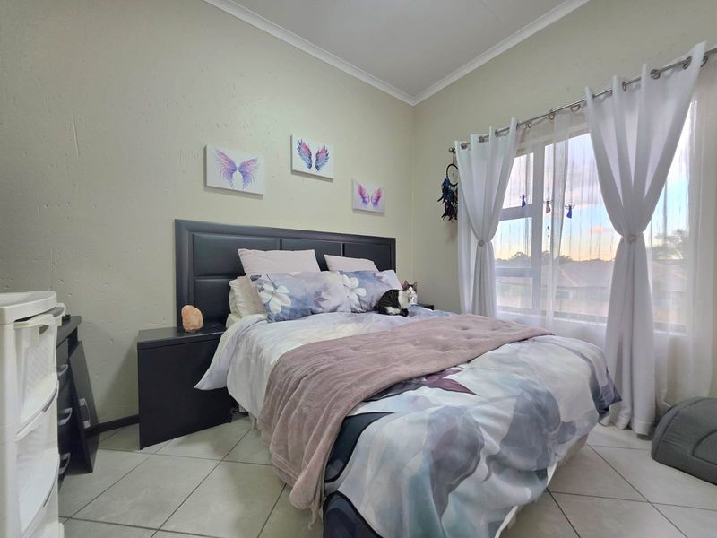 A well-lit bedroom featuring tiled flooring and a large window with curtain fixtures, providing a comfortable and functional living space.
