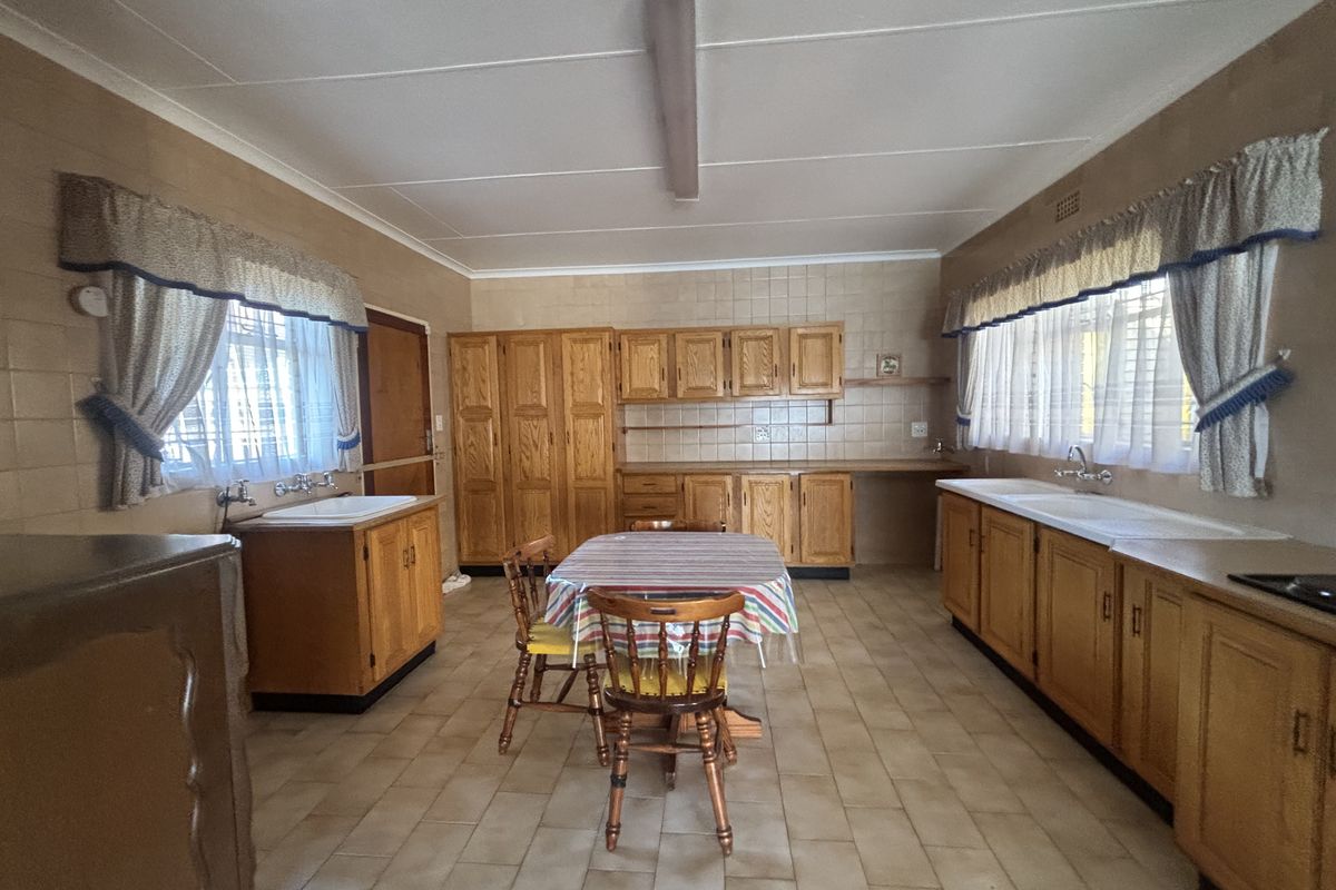 Spacious kitchen featuring extensive wooden cabinetry, tiled flooring, and dual sink areas, offering a functional layout with significant potential for modern renovation.