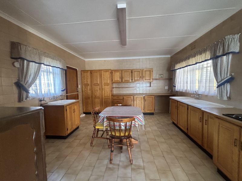 Spacious kitchen featuring extensive wooden cabinetry, tiled flooring, and dual sink areas, offering a functional layout with significant potential for modern renovation.