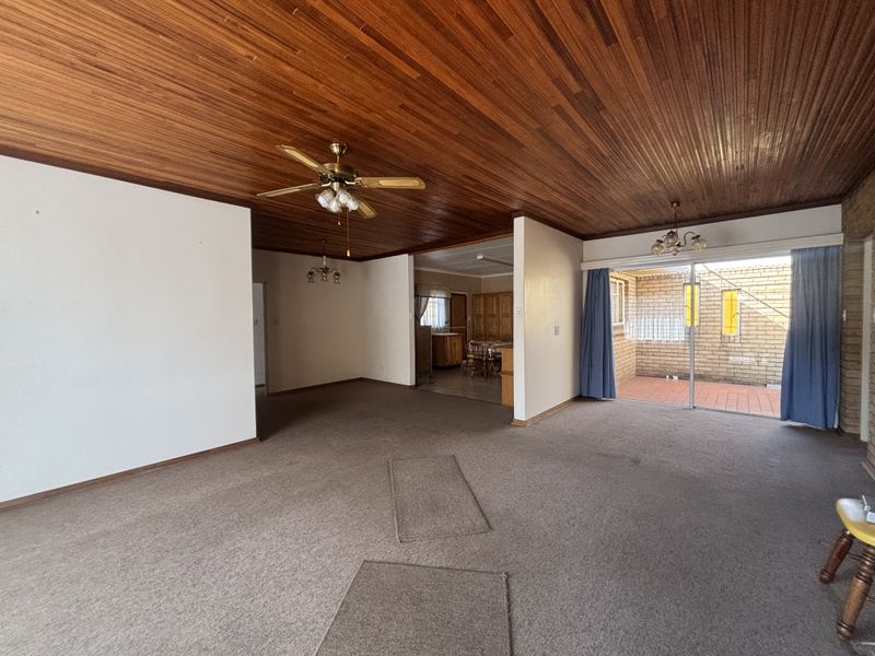 Spacious open-plan living area featuring a timber-clad ceiling, ceiling fan, and sliding glass doors leading to an outdoor patio area.