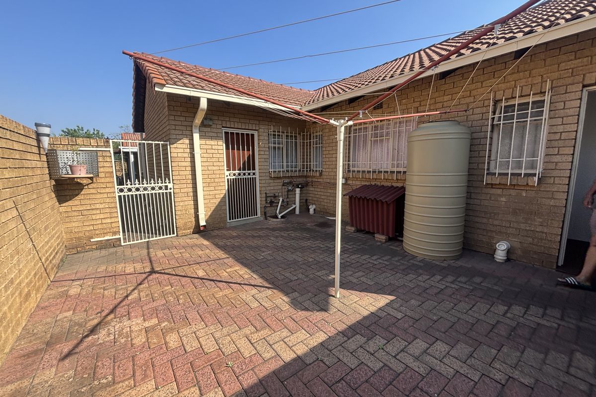 Rear courtyard area featuring brick paving, security gates, and a water storage tank against a facebrick exterior wall.