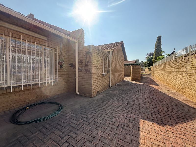 A view of the rear exterior of the house featuring face brick walls, paved flooring, and security bars on the windows.