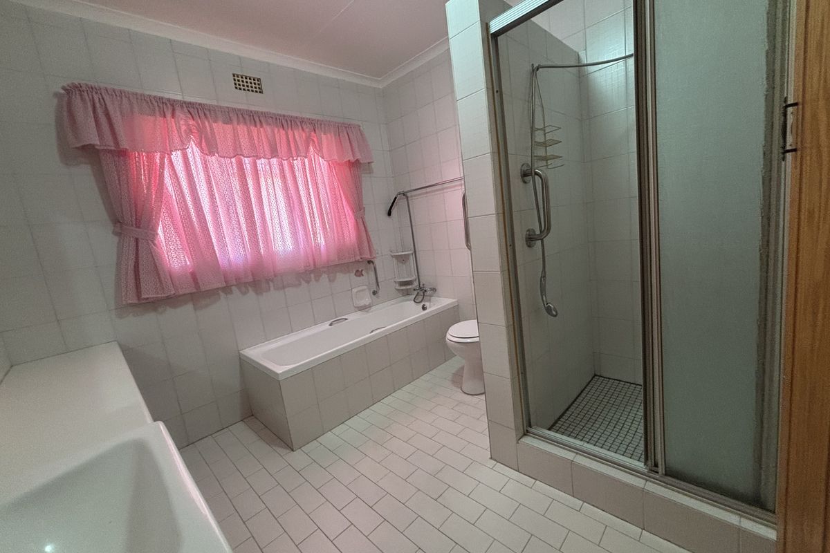 A functional bathroom featuring a built-in bathtub, separate shower enclosure, and toilet, finished with neutral wall and floor tiles.