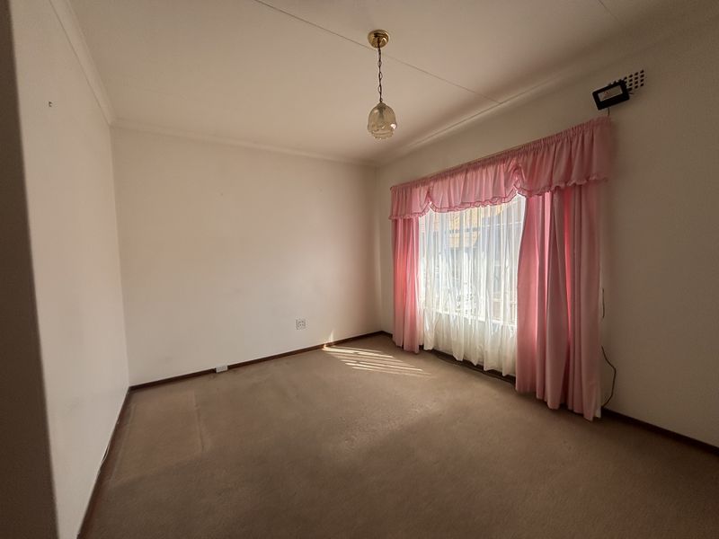 A vacant bedroom featuring carpeted flooring, cove cornicing, and a window fitted with a security grille.