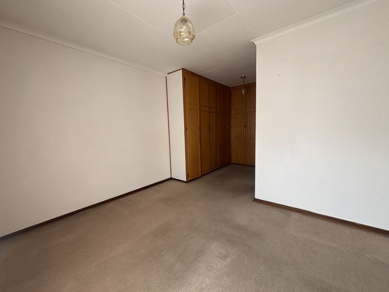 An empty bedroom featuring built-in wooden cupboards, carpeted flooring, and coved ceilings, offering a blank canvas for personalization.