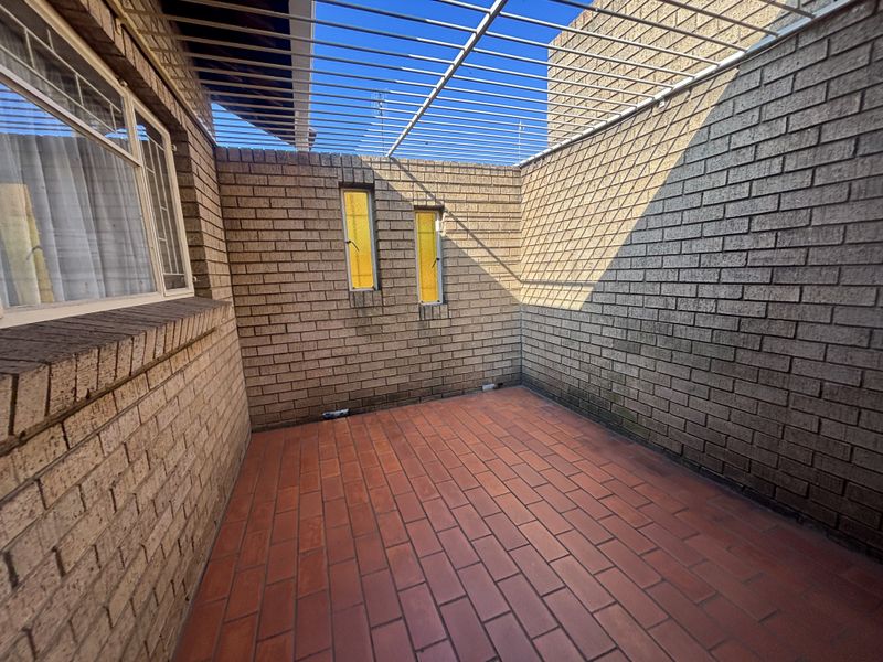 A private, enclosed patio area featuring exposed brick walls, terracotta-style floor tiles, and overhead security bars, offering a secure outdoor space.