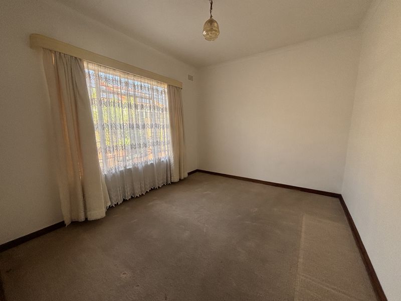 An empty bedroom featuring neutral walls, timber skirting boards, and carpet flooring, offering a blank canvas for potential updates or staging.