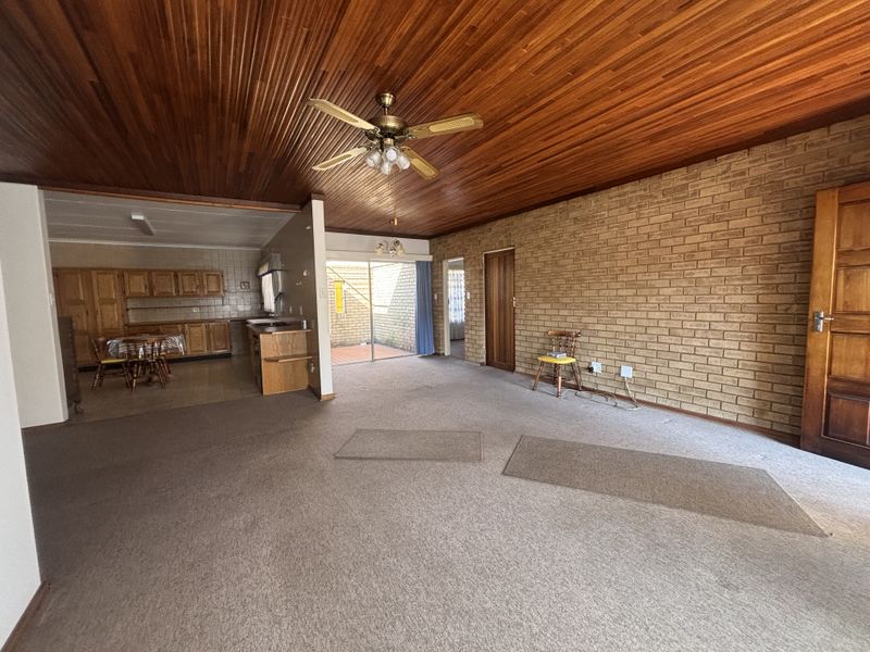 Spacious open-plan living and kitchen area featuring a distinctive timber ceiling, exposed brick wall, and direct access to an outdoor patio space.
