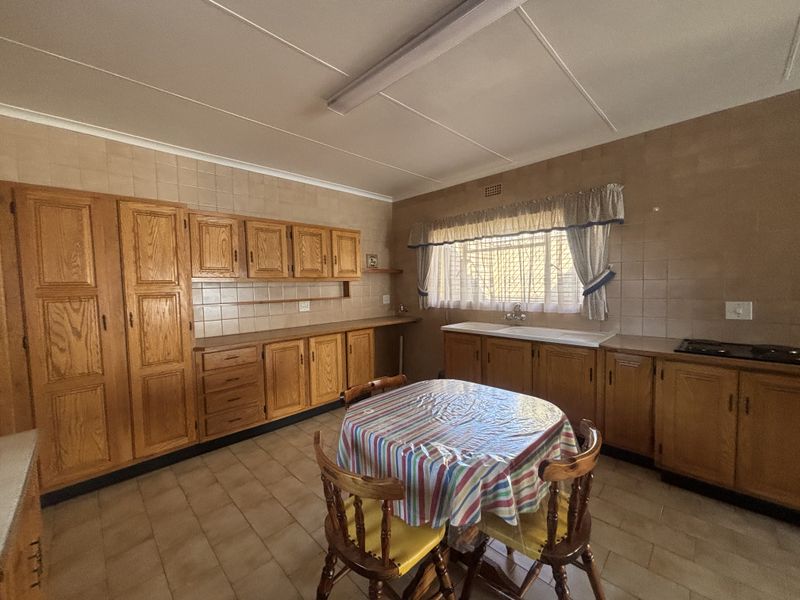 A spacious kitchen featuring extensive wooden cabinetry, tiled backsplash, and a functional layout with a built-in hob and double sink.