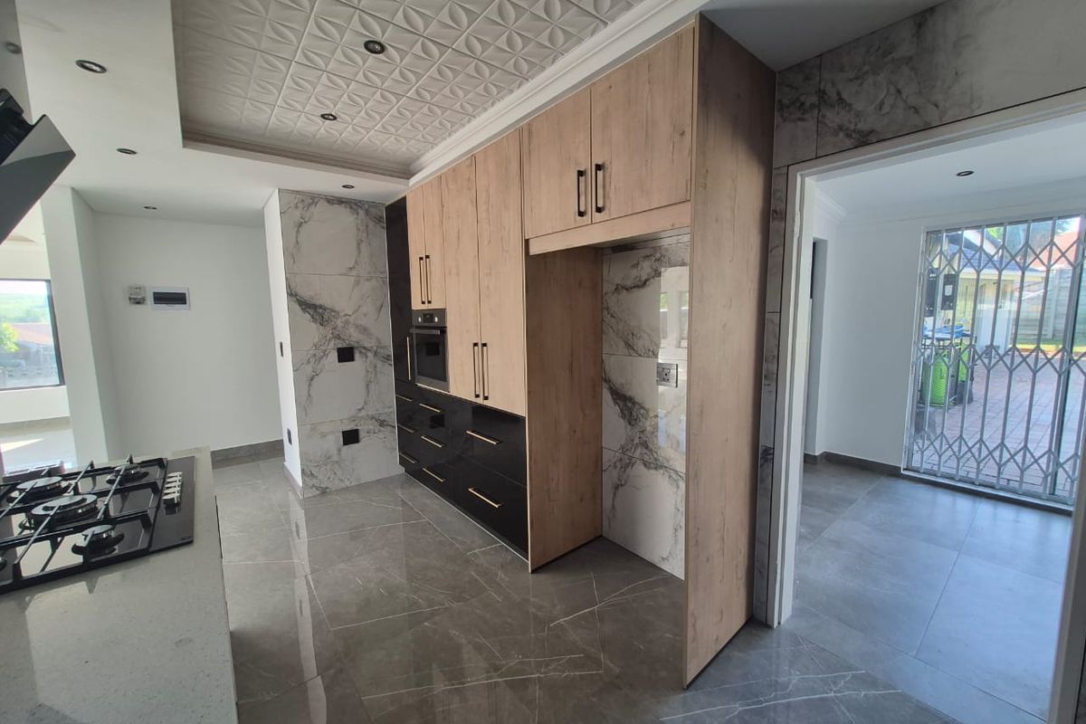 Modern kitchen featuring high-end marble-look finishes, sleek two-tone cabinetry, built-in oven, gas hob, and large-format porcelain floor tiles.
