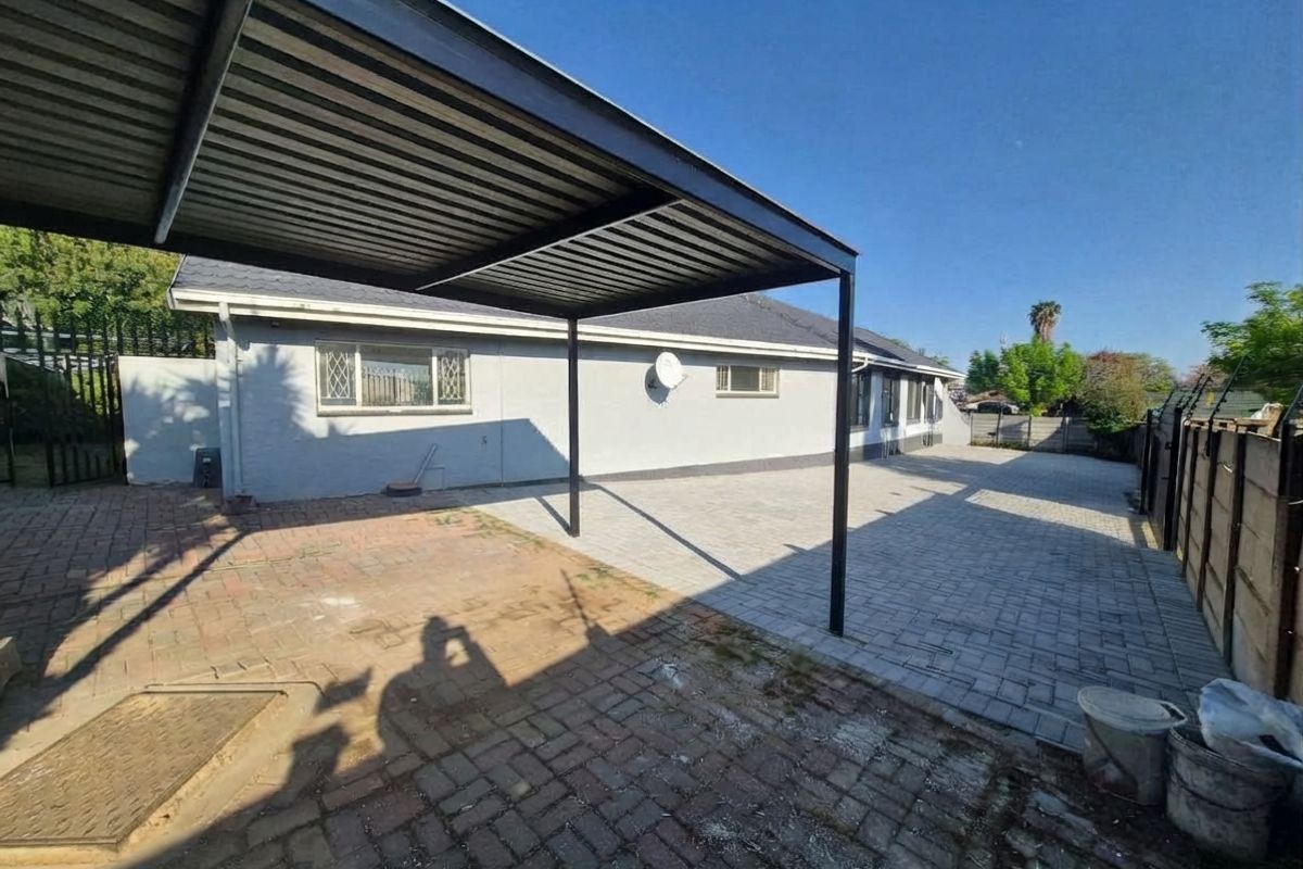 Rear exterior area featuring a metal carport structure and extensive paved surfacing, providing a functional outdoor space.