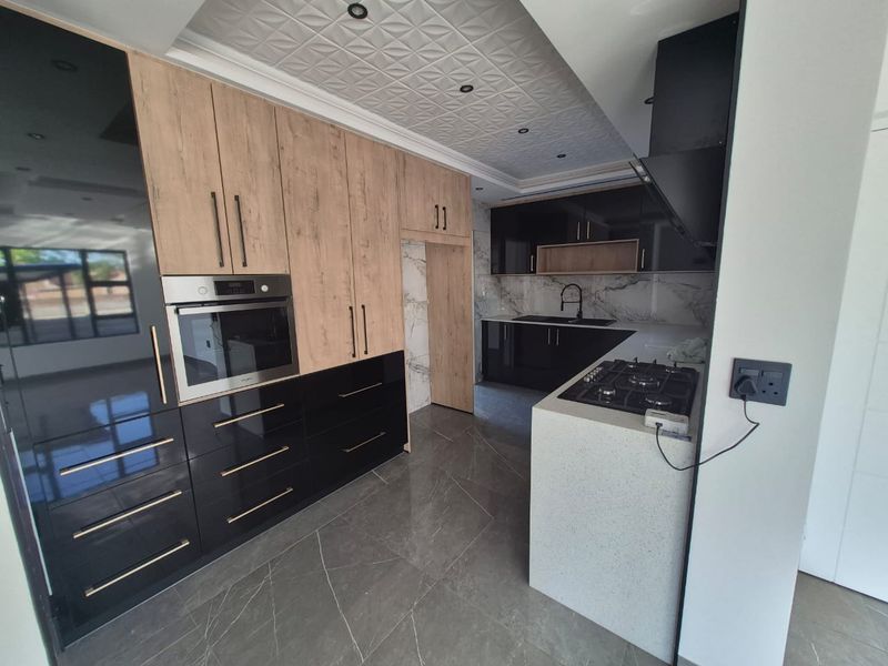 Modern kitchen featuring high-contrast black and wood-grain cabinetry, stone countertops, built-in oven, gas hob, and elegant marble-look splashback with recessed ceiling detail.