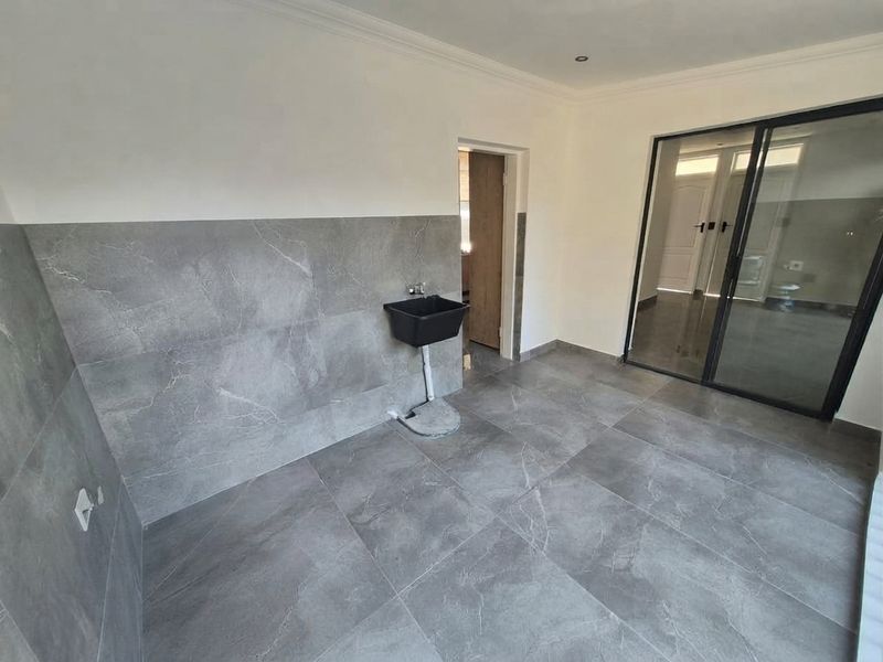 A clean, modern laundry area featuring large-format grey marble-look floor and wall tiles, a utility sink, and a sliding glass door.