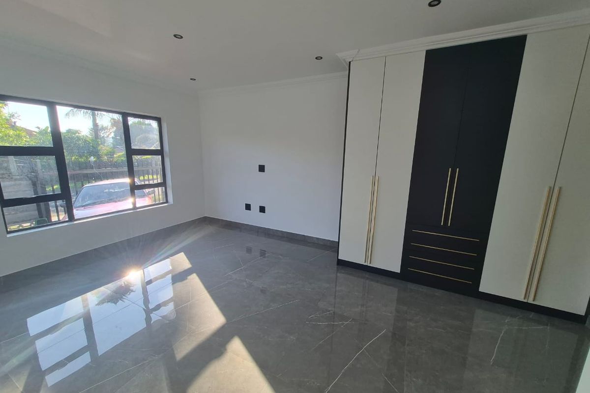 A modern, empty bedroom featuring high-gloss tiled flooring, recessed downlighting, and contemporary built-in cupboards with contrasting black and white finishes.