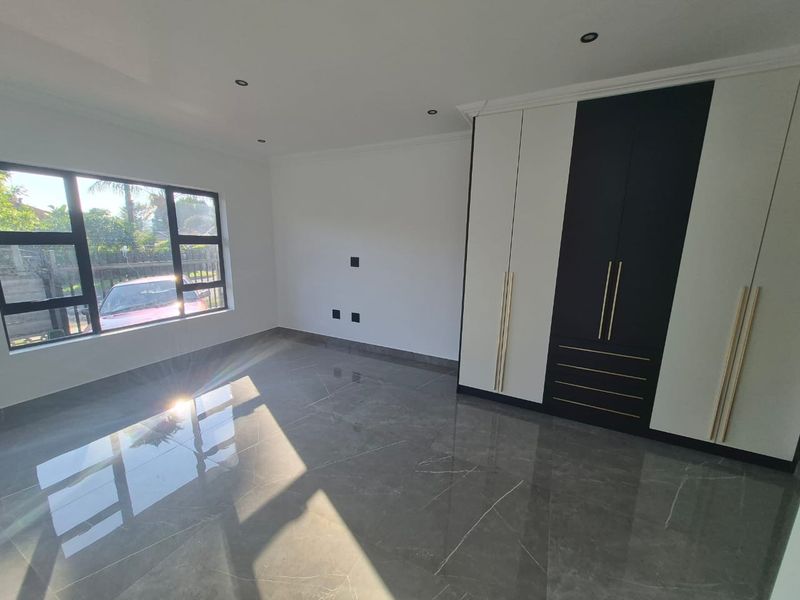 A modern, empty bedroom featuring high-gloss tiled flooring, recessed downlighting, and contemporary built-in cupboards with contrasting black and white finishes.