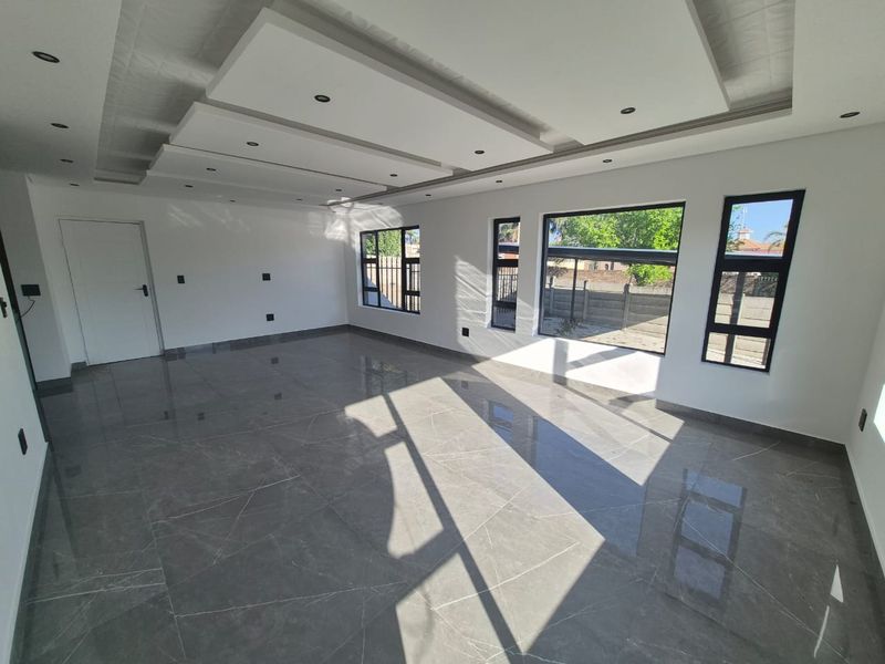 A bright, spacious, and empty living area featuring modern recessed ceiling details, downlights, and large porcelain floor tiles with aluminium-framed windows.