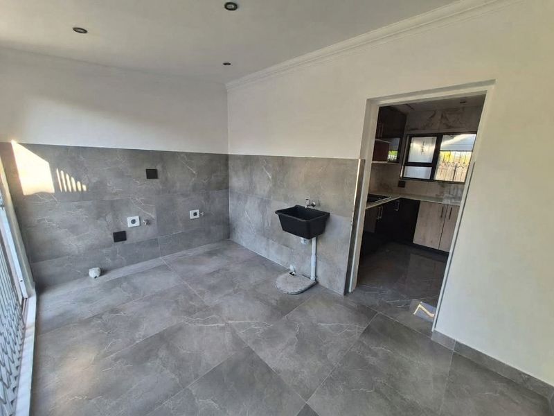 A clean, modern scullery area featuring grey porcelain tiling throughout, a wall-mounted utility sink, and direct access to the adjoining kitchen.