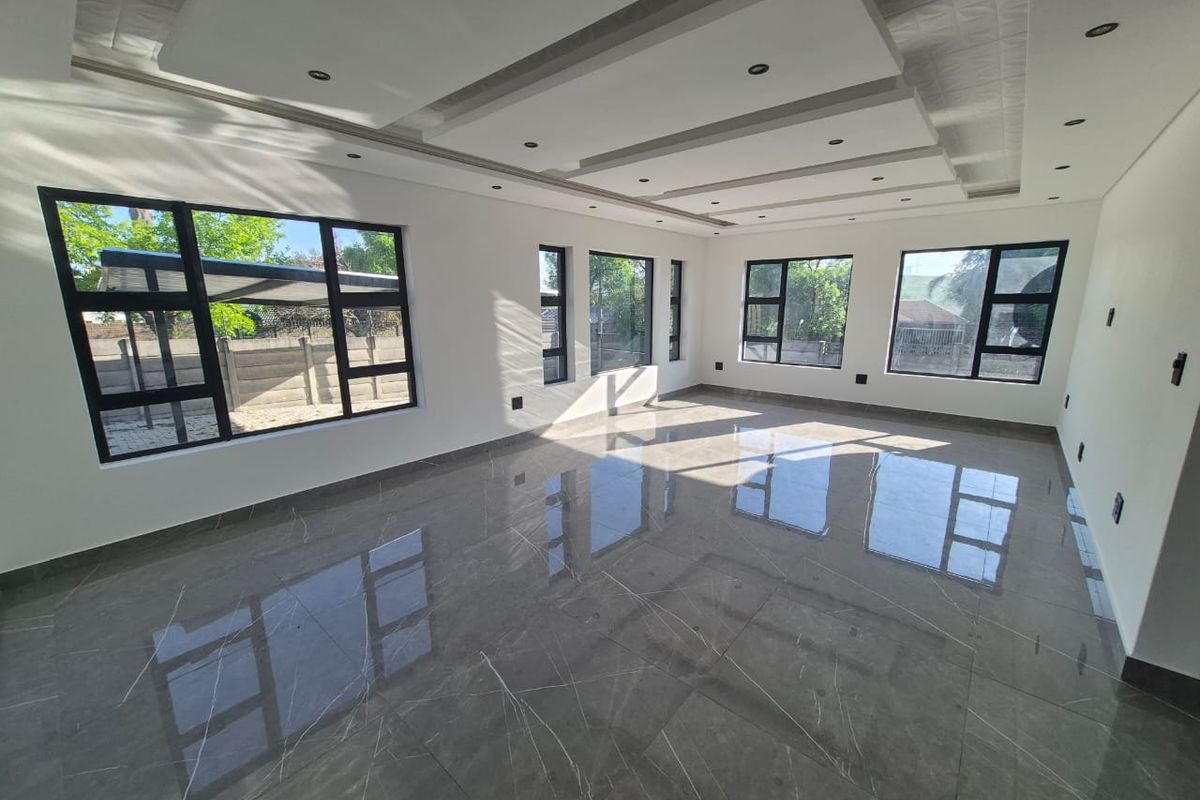 A bright and spacious living area featuring modern porcelain floor tiles, a decorative recessed ceiling with downlights, and large aluminium-framed windows.