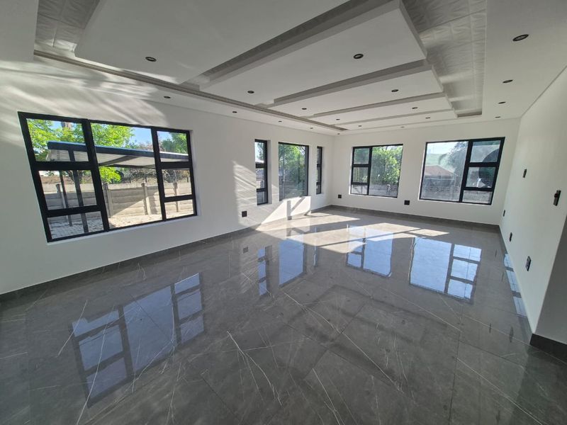 A bright and spacious living area featuring modern porcelain floor tiles, a decorative recessed ceiling with downlights, and large aluminium-framed windows.