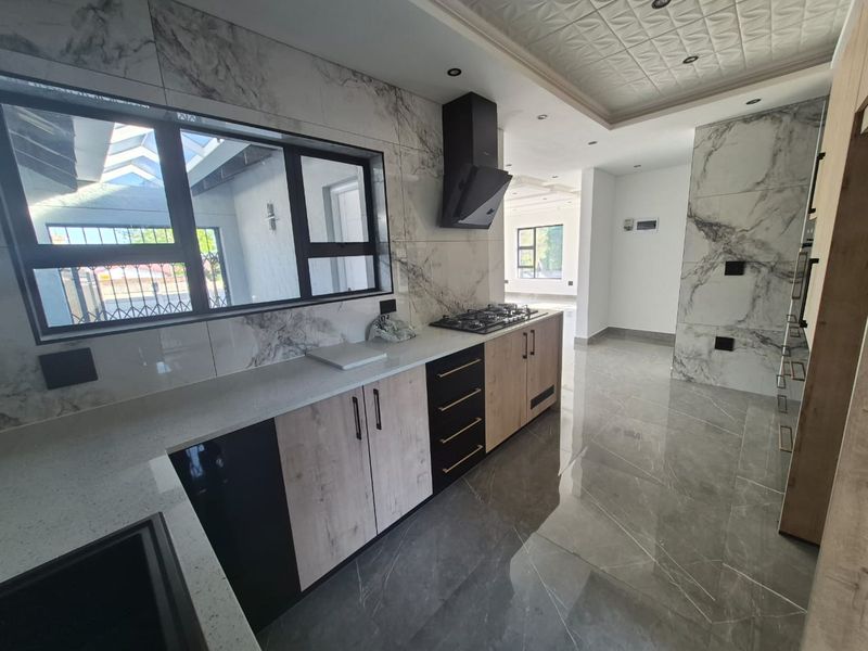 Modern kitchen featuring marble-look wall tiles, stone countertops, gas hob with extractor fan, and sleek two-tone cabinetry in an open-plan layout.
