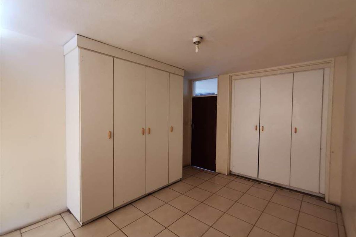 A bedroom featuring extensive built-in cupboard storage, tiled flooring, and a simple entrance door.