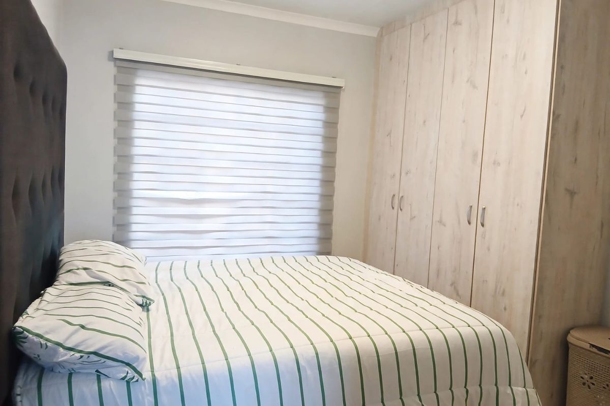 A well-maintained bedroom featuring light wood-finish built-in cupboards and modern roller blinds, providing a clean and functional living space.