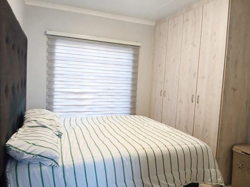 A well-maintained bedroom featuring light wood-finish built-in cupboards and modern roller blinds, providing a clean and functional living space.