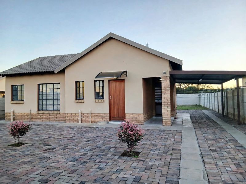 A well-maintained single-story house featuring a brick-paved driveway, a covered carport, and a neat facade with a tiled roof and secure entrance.