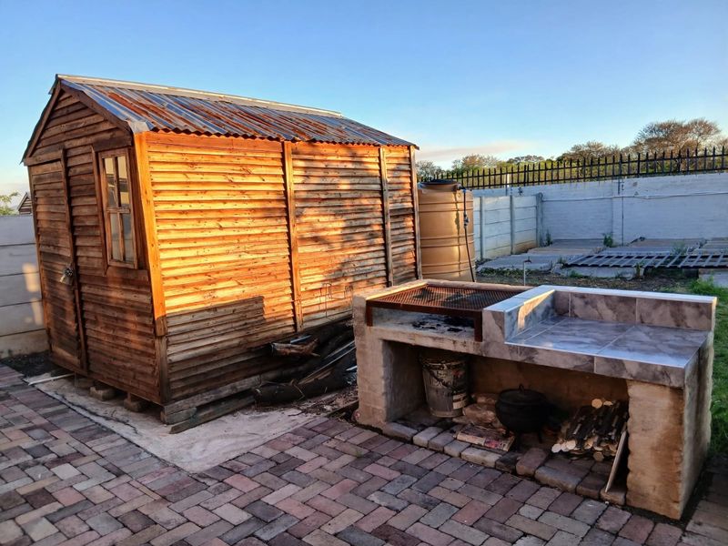 Rear garden area featuring a timber storage shed, a built-in brick braai with tiled prep surface, and a water storage tank on a paved patio.