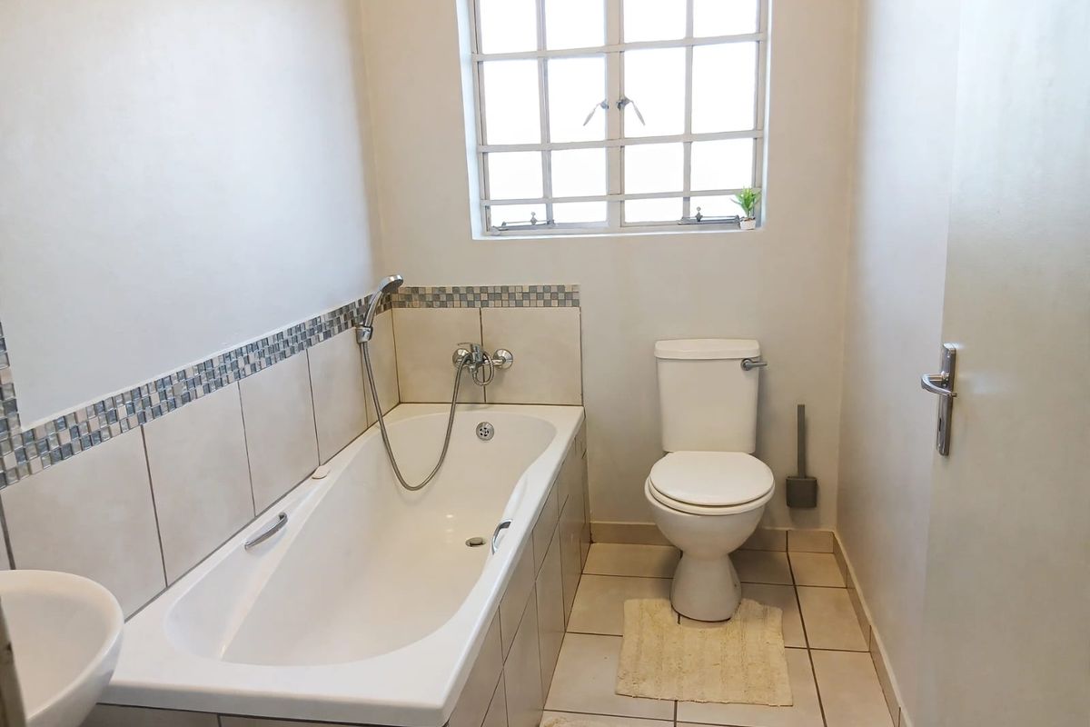 A functional bathroom featuring a bathtub with shower attachment, a toilet, and a basin, finished with neutral wall and floor tiles.